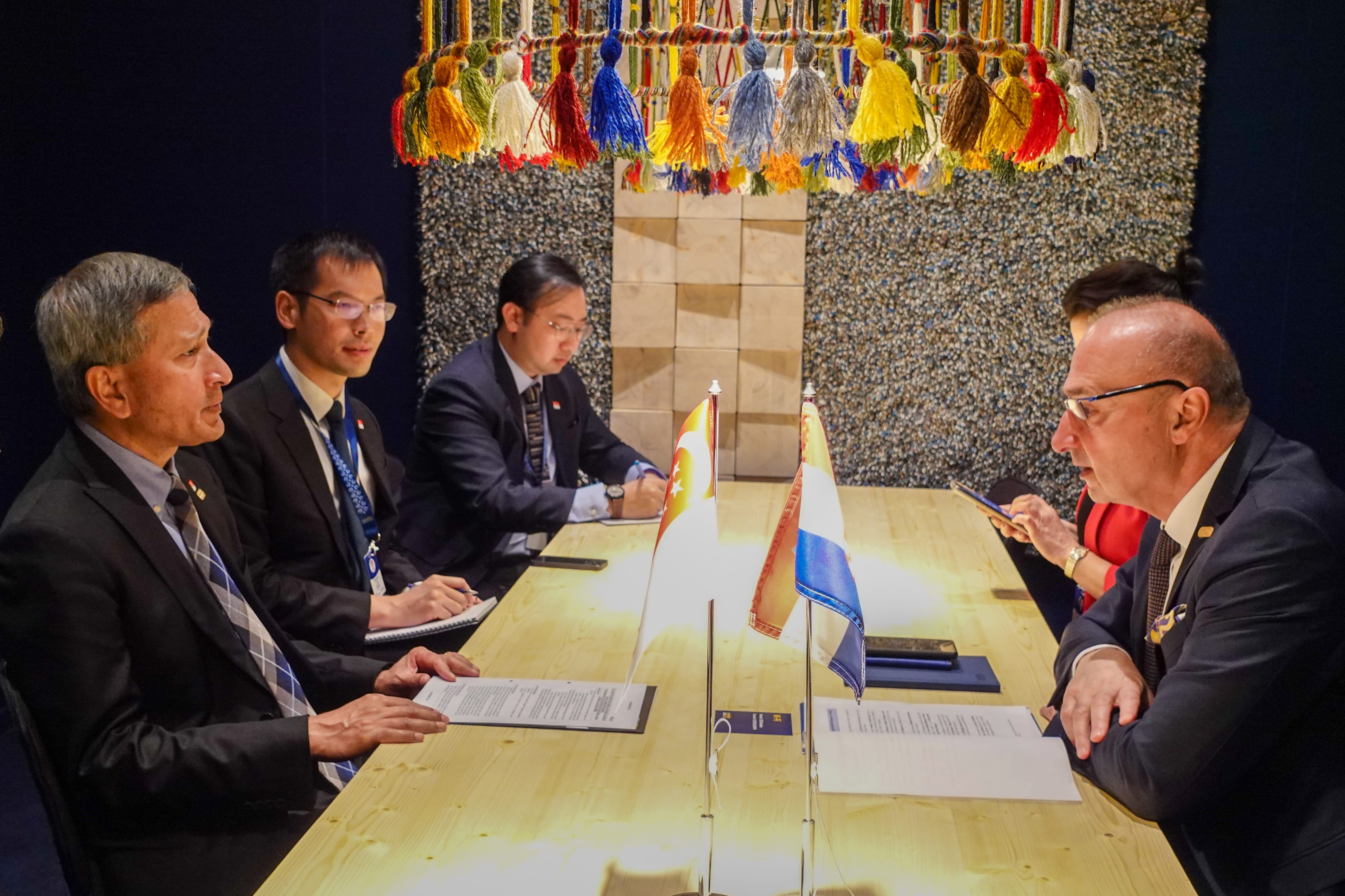 People in suits at a table with Singapore and Dutch flags and a document.